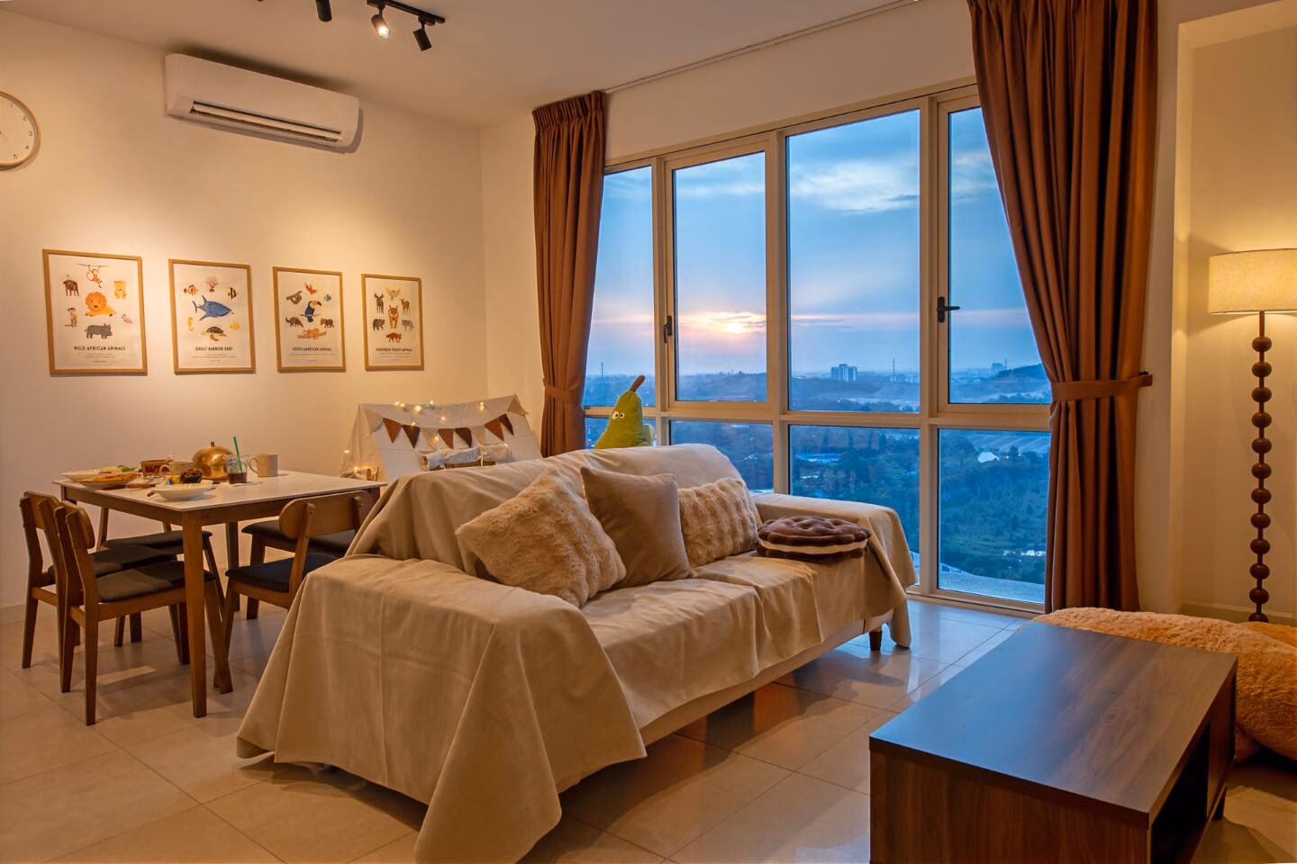 Living room of a two-bedroom apartment RoomGuru manages at Afiniti in Medini, styled for families, with the sunset over Iskandar Puteri through full-height windows