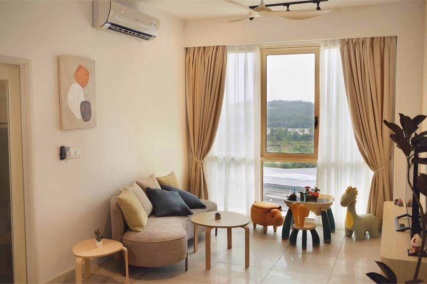 The living room of a Medini apartment let nightly, with a sofa, a low table, a toddler-sized table and chairs and soft toys by the window.